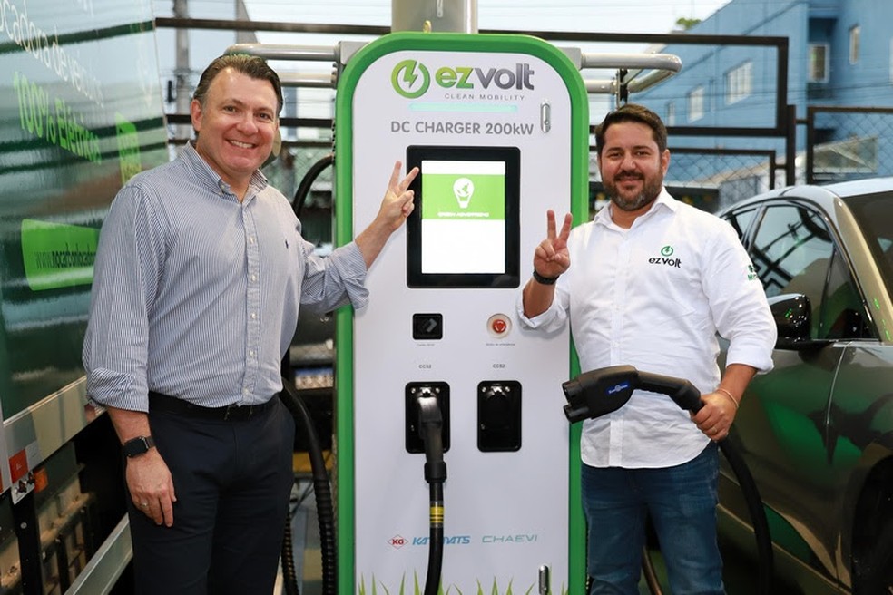 Gustavo Tannure, CEO da EZVolt e Bernardo Kos Winik, executivo da Vibra, ao lado de um carregador ultrarrápido — Foto: Divulgação